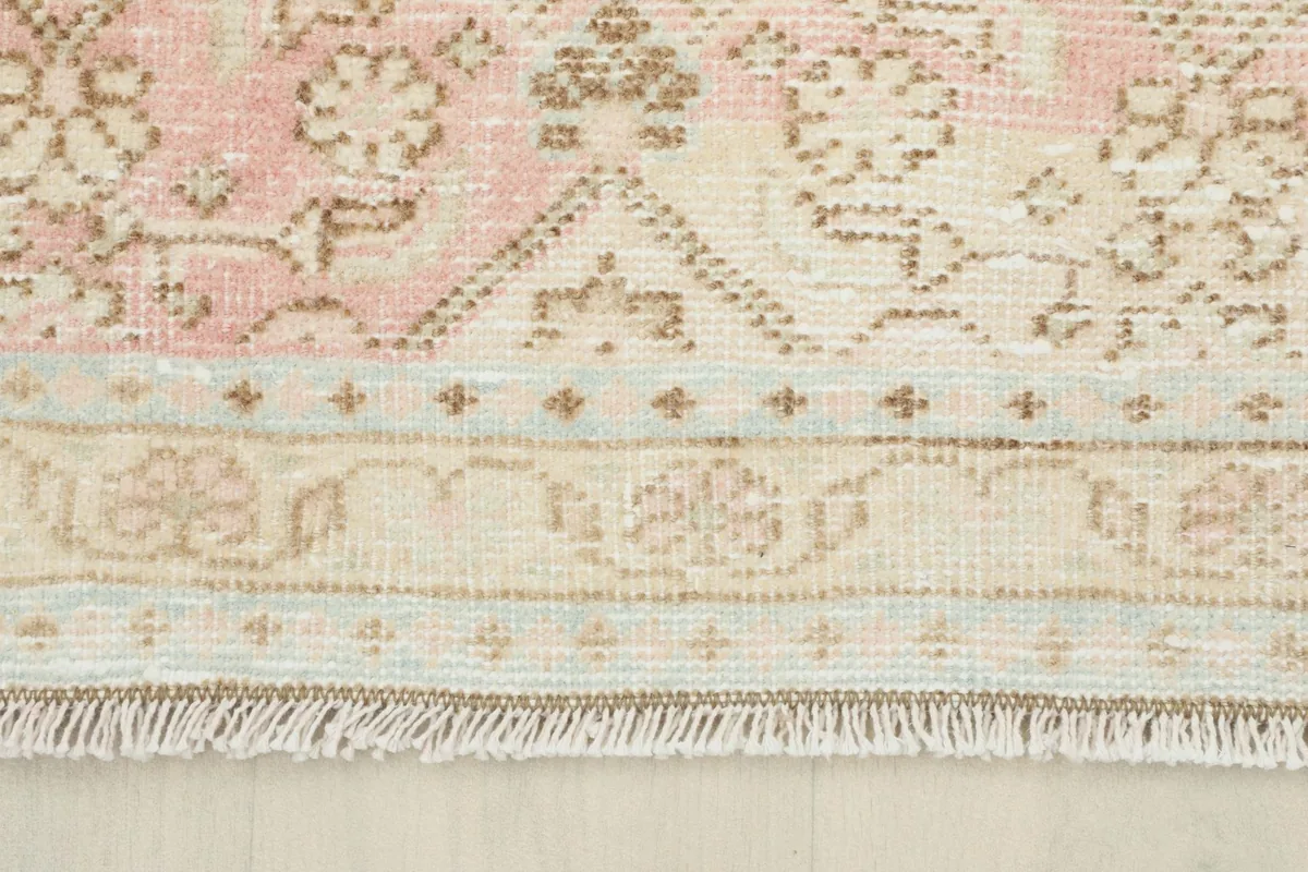 Close-up of the rug's border, showing the subtle rose and cream color variations and fringe.