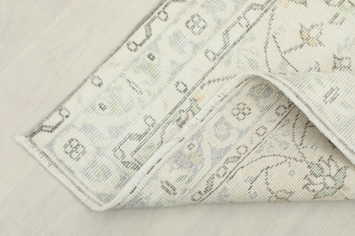 Corner of the ivory rug folded to show the back of the cotton foundation and knotting