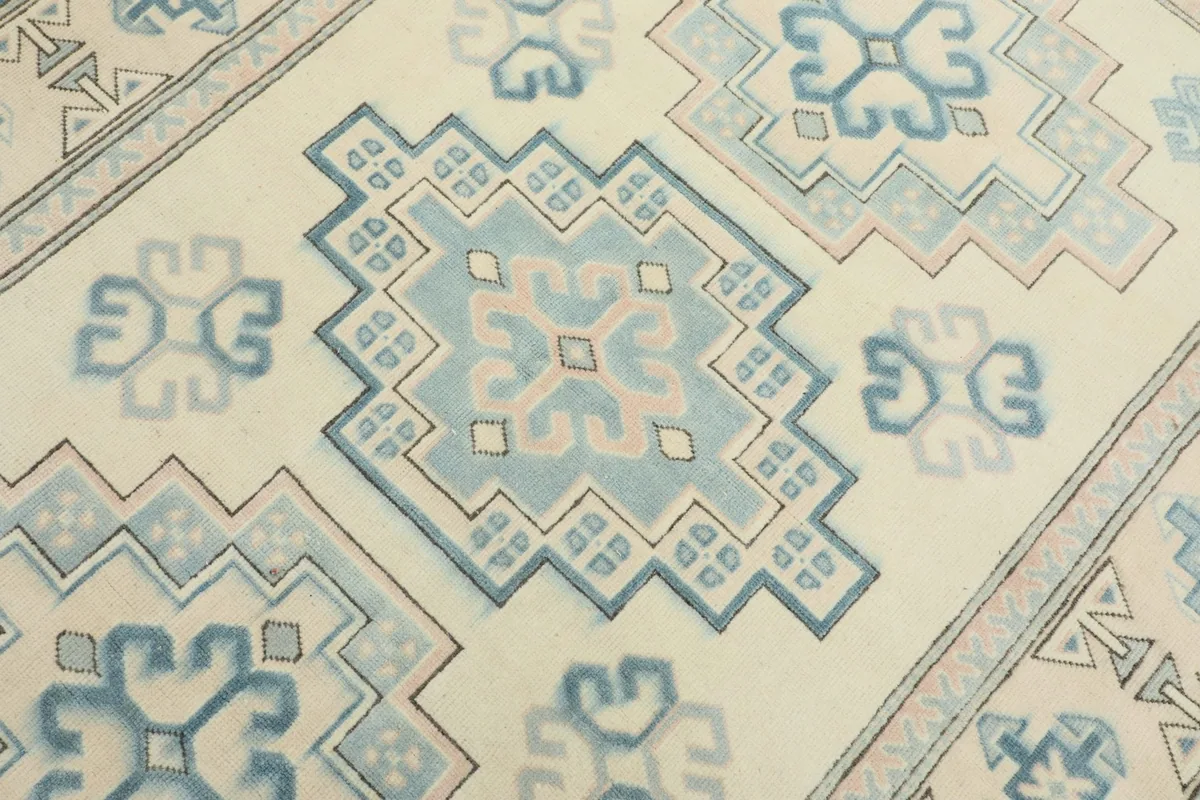 Detailed view of a central geometric motif in shades of blue and rose on the ivory field.