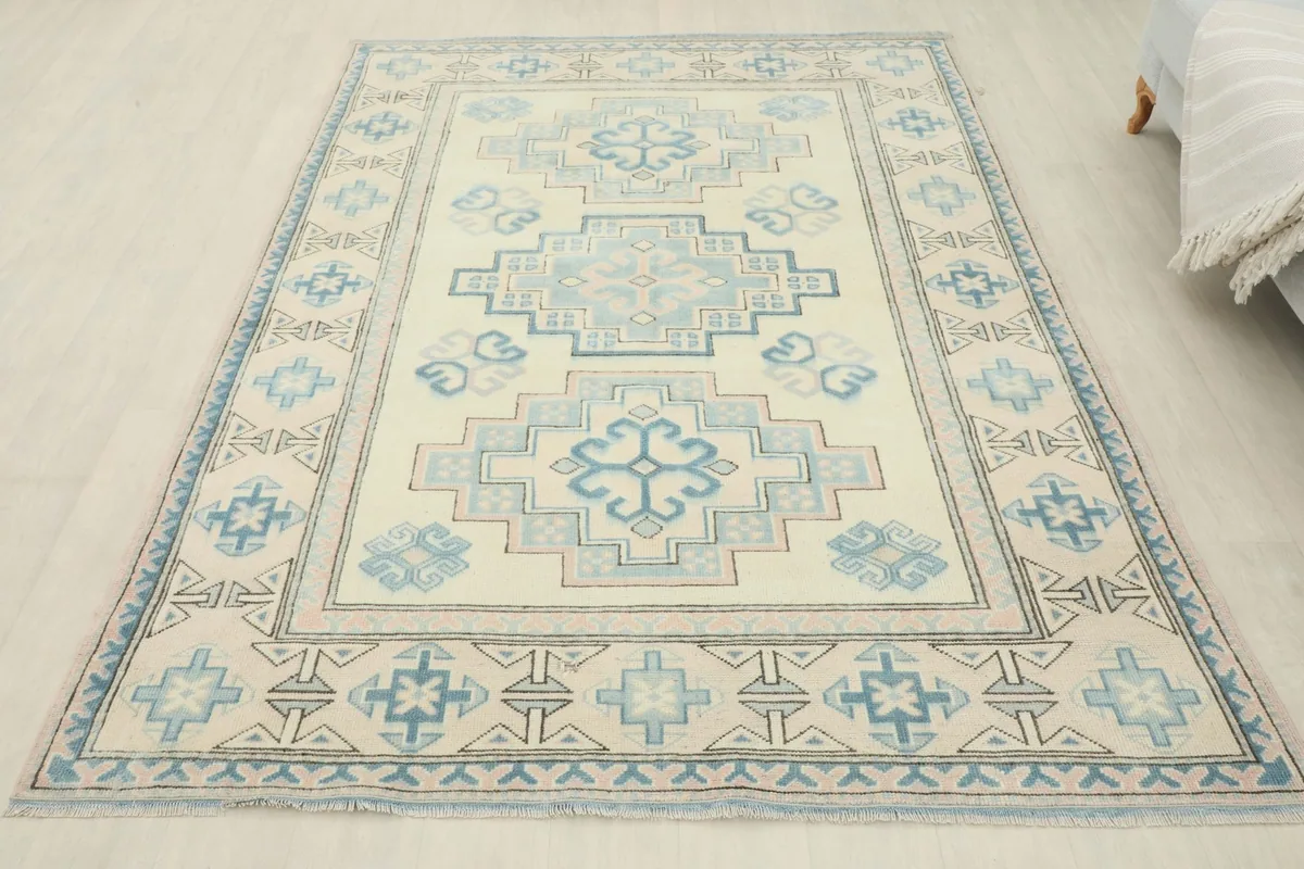 Full overhead view of the vintage ivory, blue, and rose rug laid out on a light floor.