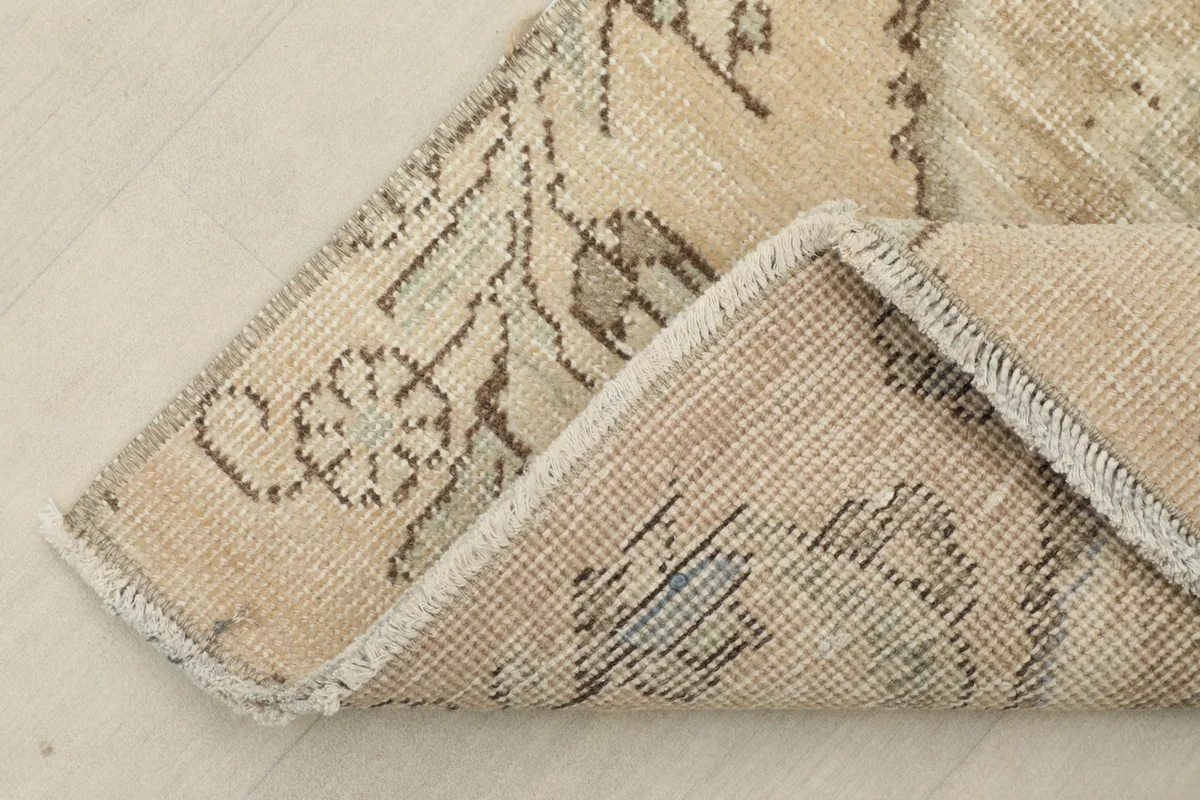 View of the rug's corner folded back, showing the cotton foundation and the reverse of the knots.