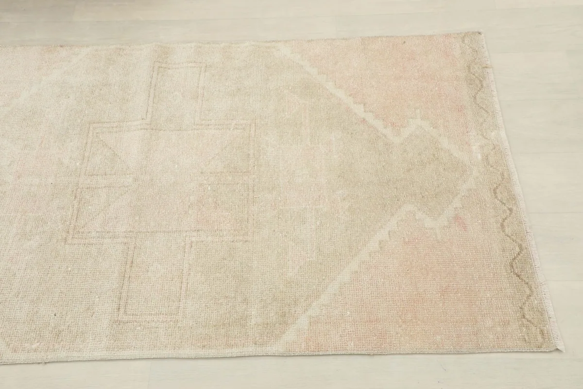 Close-up view of one end of the runner rug, showing subtle rose tones and geometric motifs.