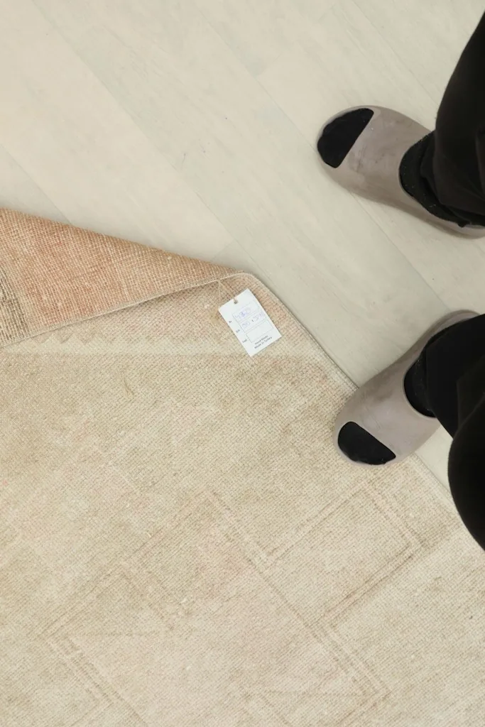 Overhead view of a person's feet near the rug, with a tag visible on the folded corner.