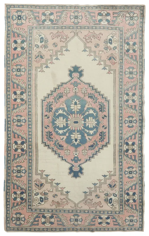 Full top view of the vintage Anatolian rug with ivory field, pink and blue medallion, and geometric border.