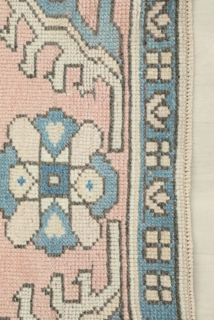 Detail of the rug's border, displaying the repeating blue and pink motifs and the edge finishing.