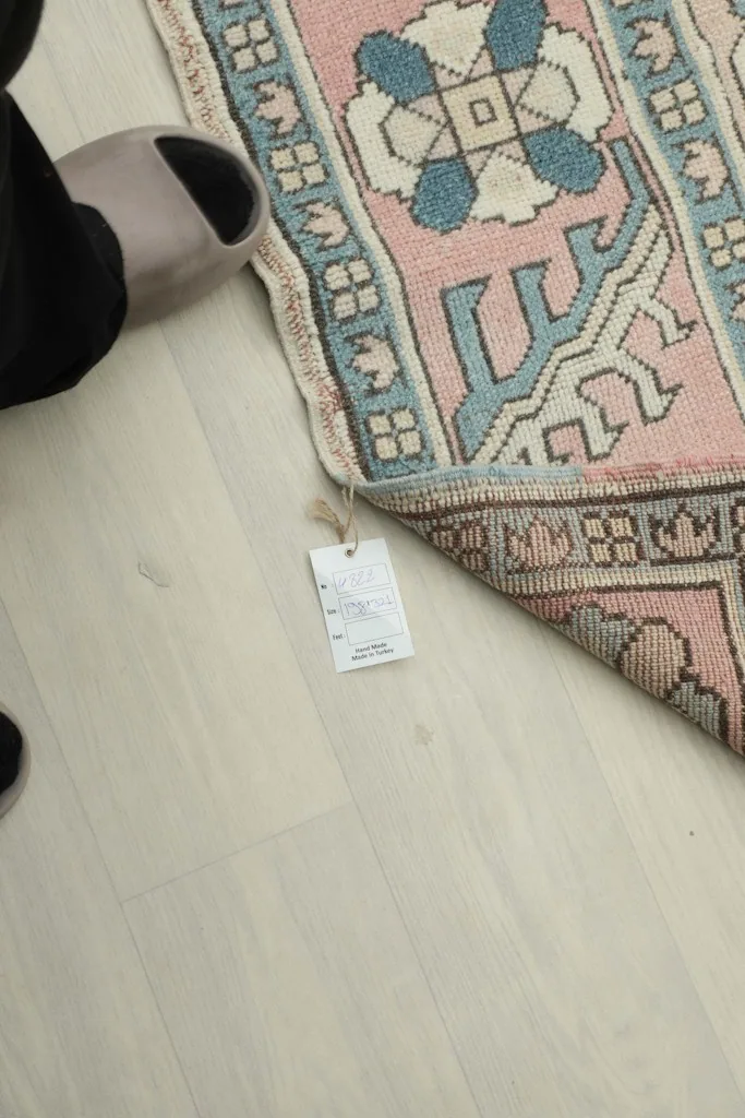 A foot in a slipper next to a corner of the rug, showing a tag attached to the rug's edge.