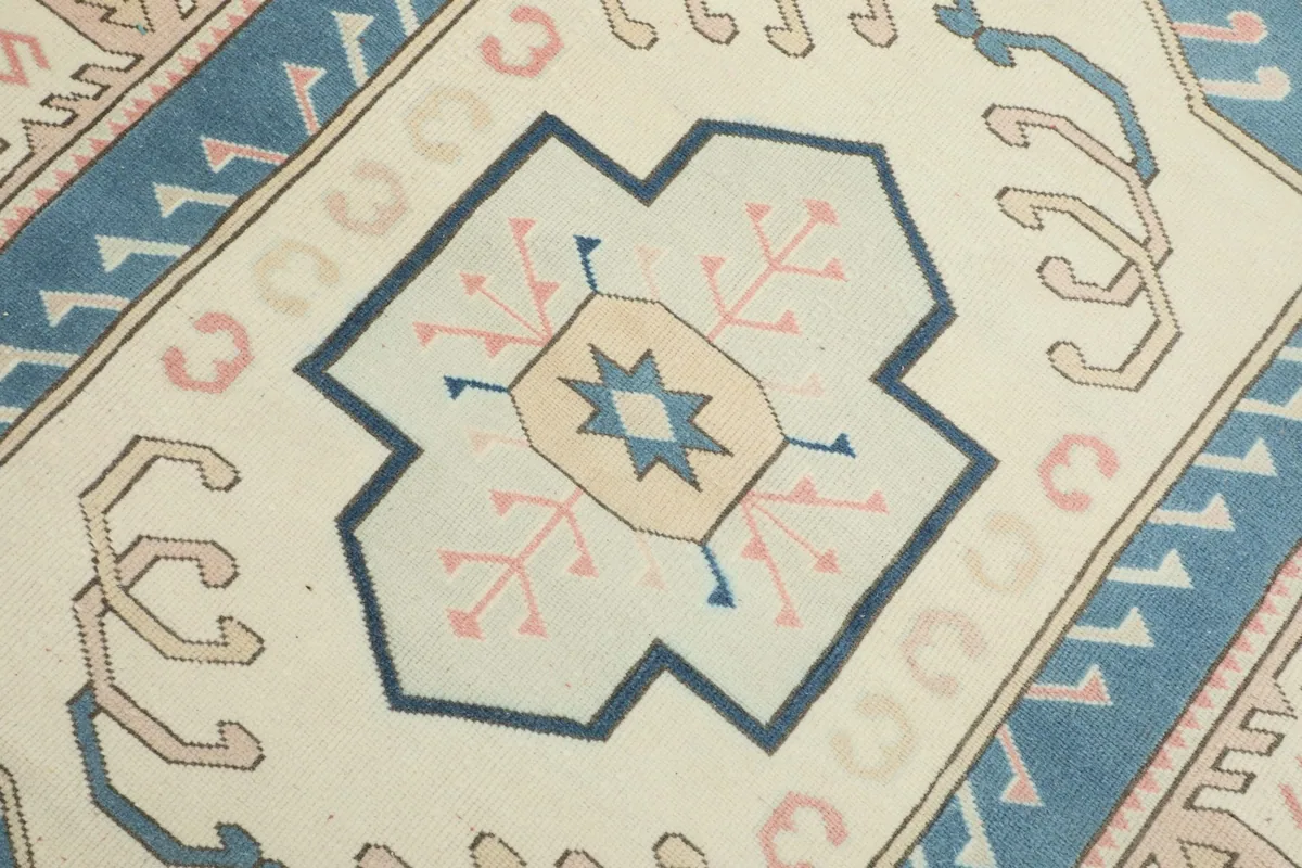 Close-up of the central medallion motif with blue, rose, and tan details on an ivory background.