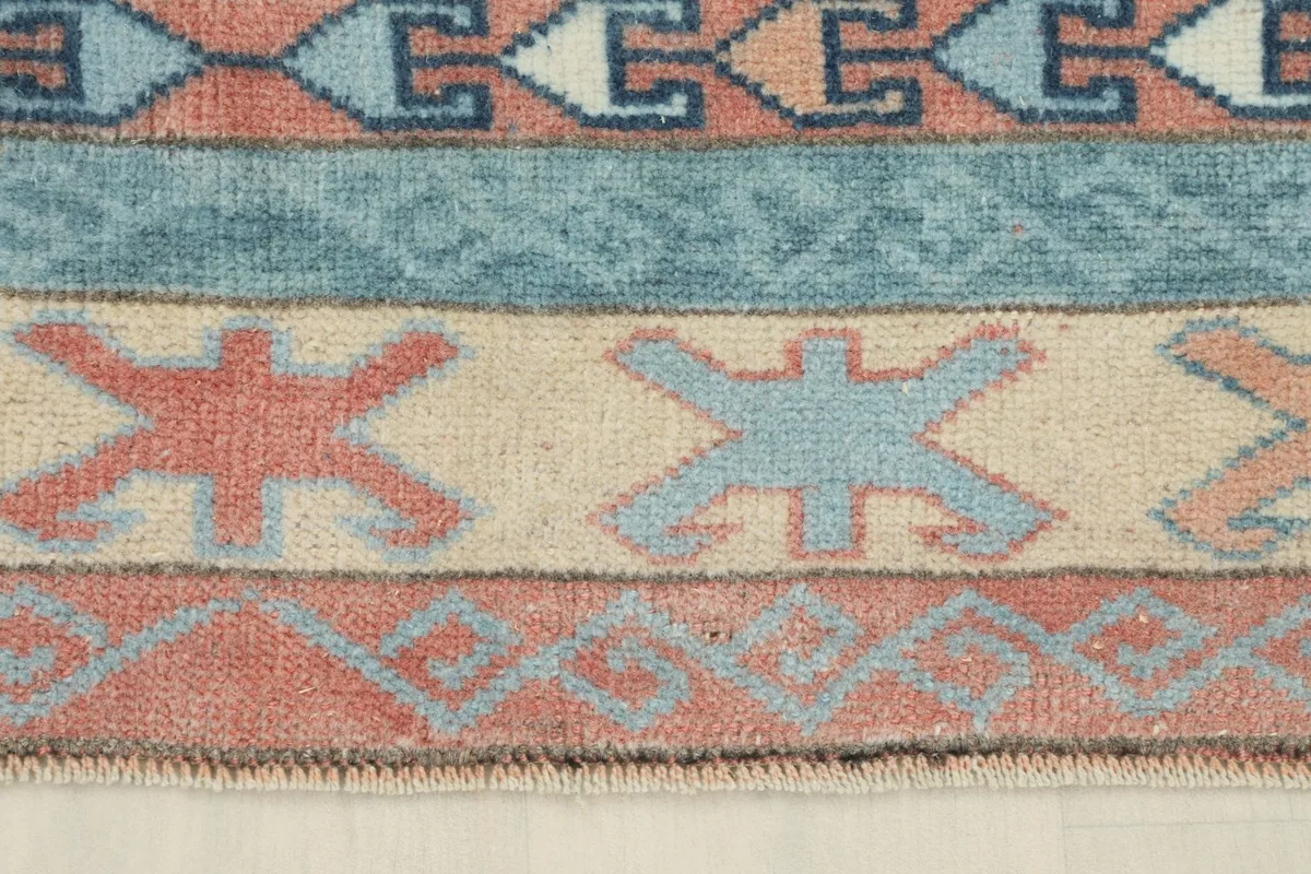 Detailed section of the border showing rust and blue tribal figures on a beige ground
