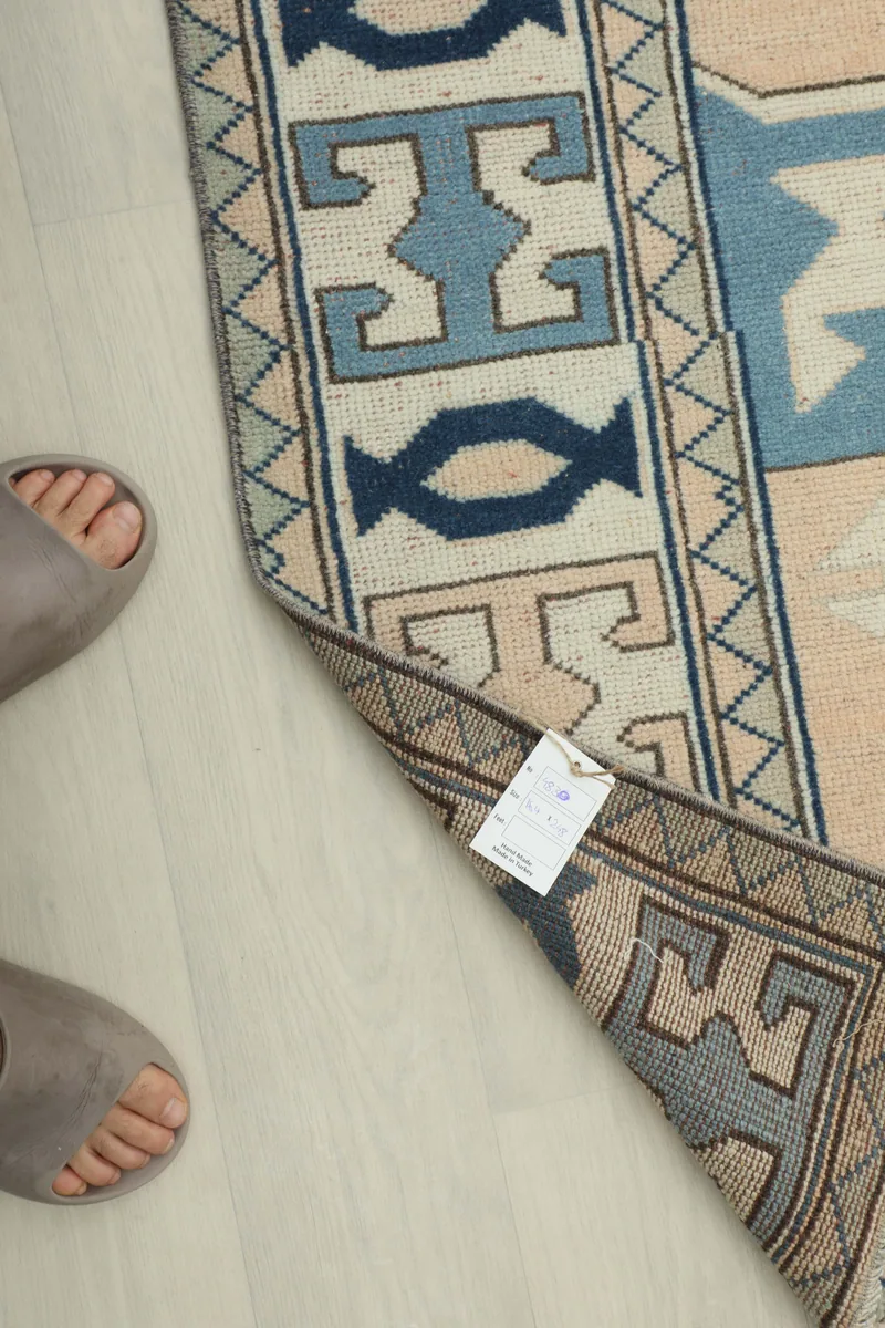 Corner of the Cream Blue Geometric Anatolian Rug with a tag, next to feet for scale