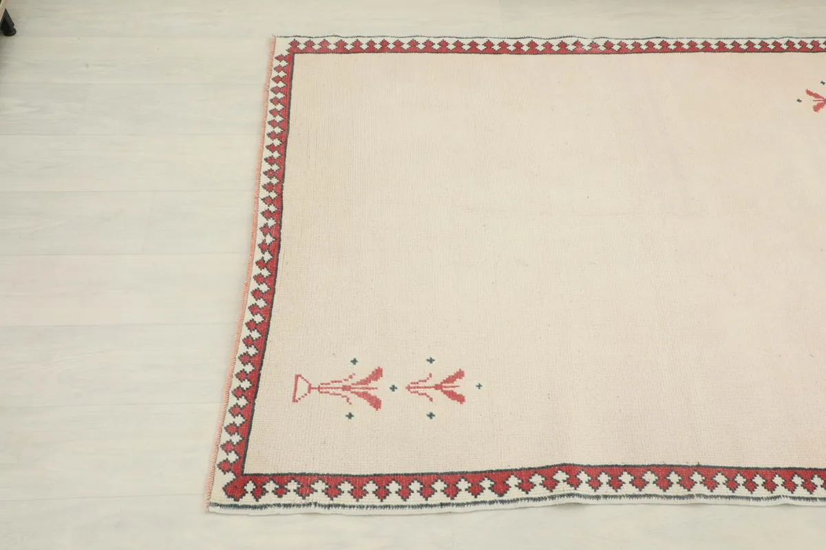 Close-up angle view of the lower left corner of the vintage rug showing a red floral motif