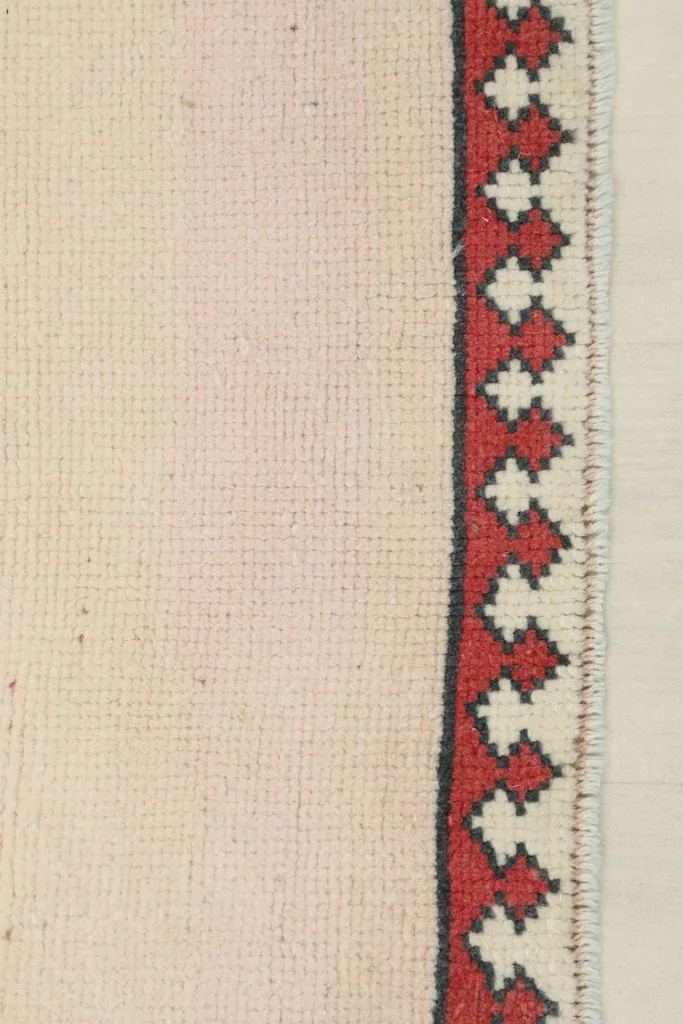 Close-up of the red and ivory geometric border with a thin charcoal outline on the rug's edge