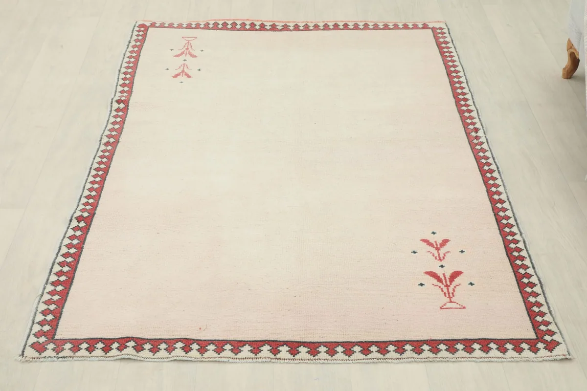 Full overhead view of the ivory rug, highlighting the red border and corner motifs