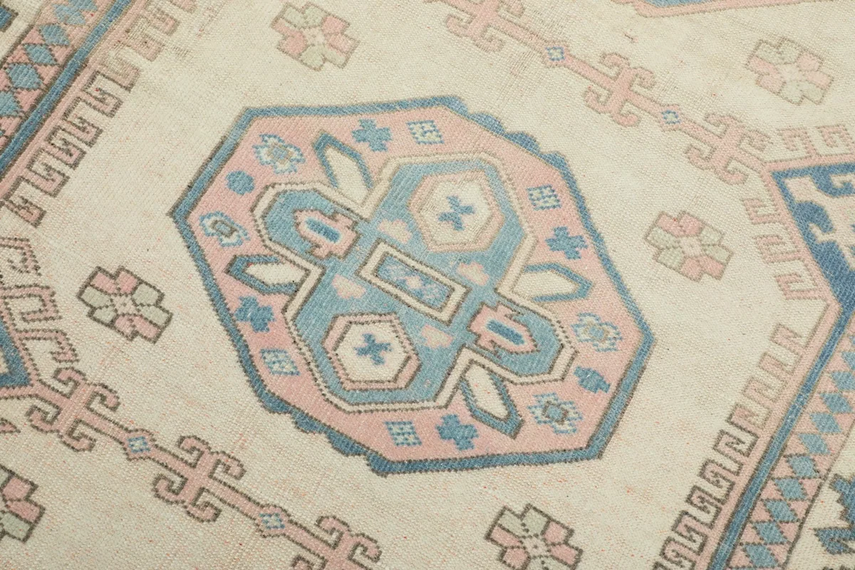 Detailed view of a central medallion motif with blue and pink geometric shapes on an ivory field.
