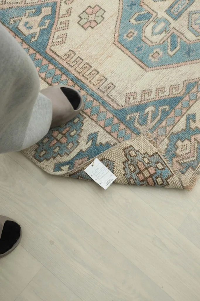 Foot in a slipper next to a folded corner of the rug, showing scale and the attached product tag.