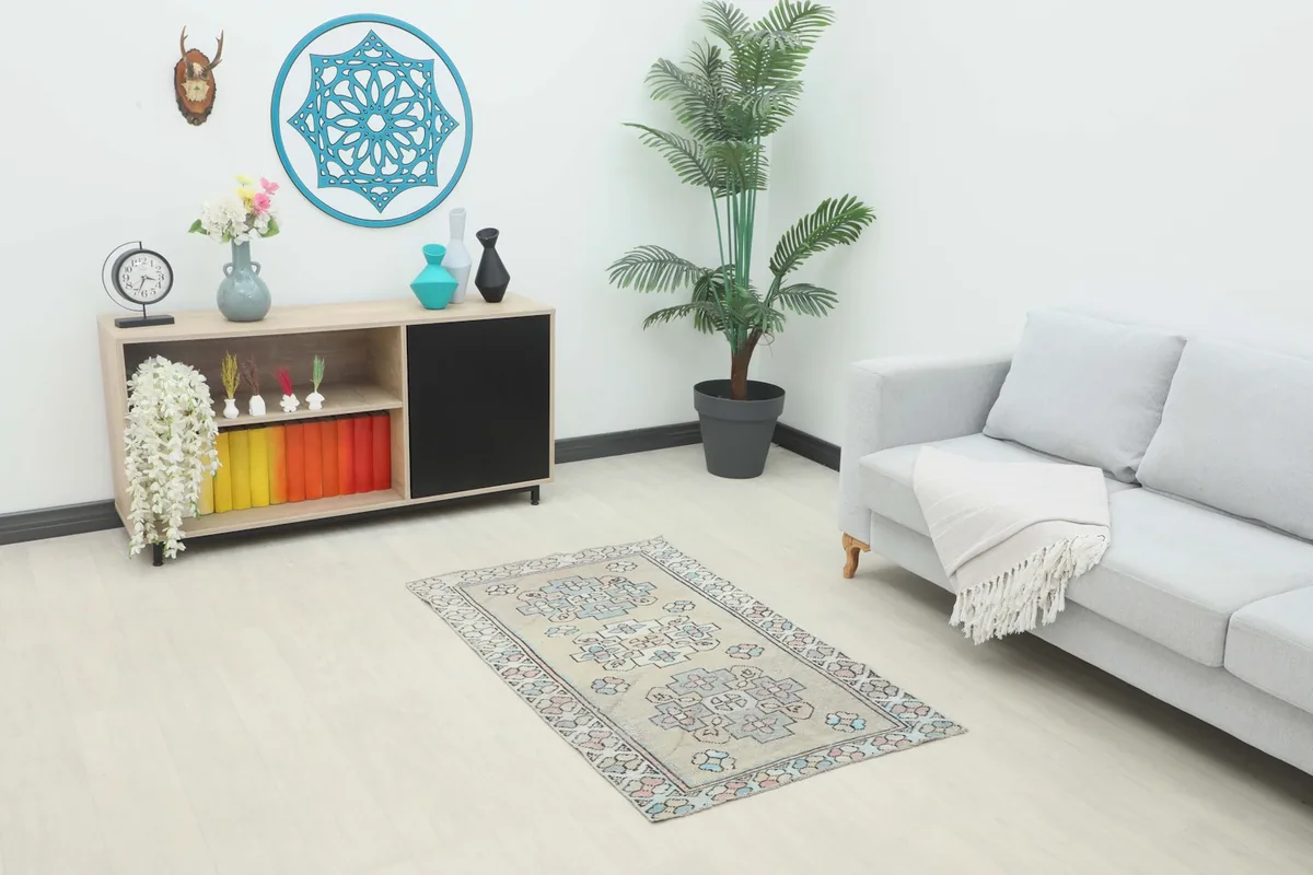 Vintage beige, rose, and blue rug displayed in a modern living room setting with a sofa and cabinet.
