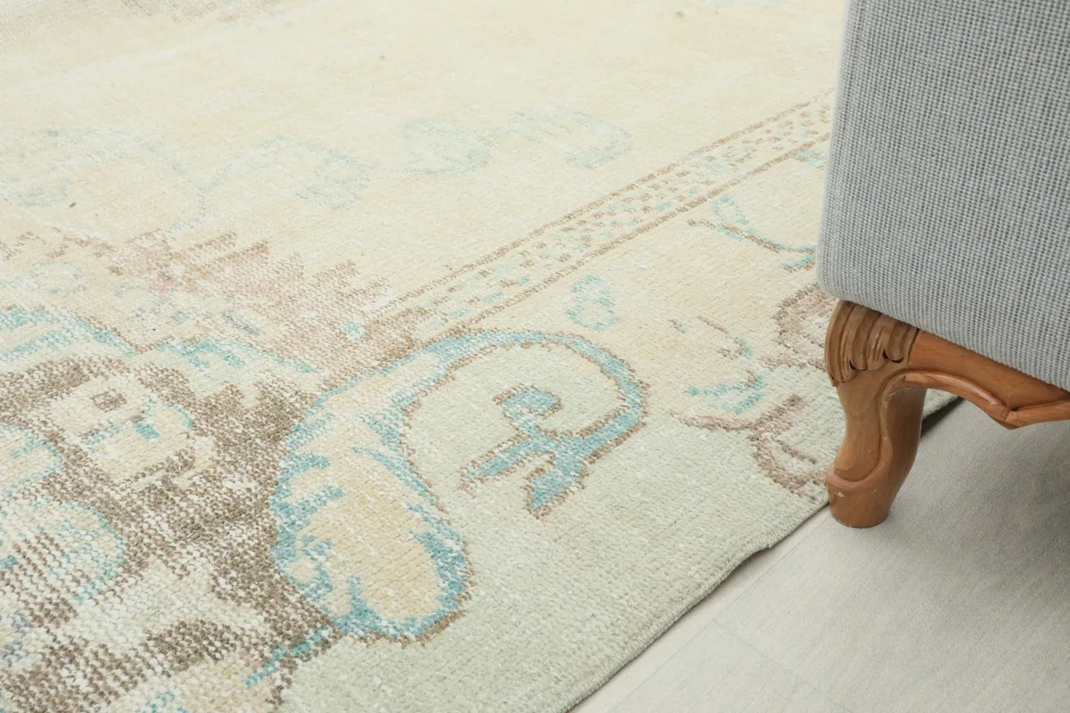 Corner detail of the rug's border and faded motif, with a furniture leg for scale