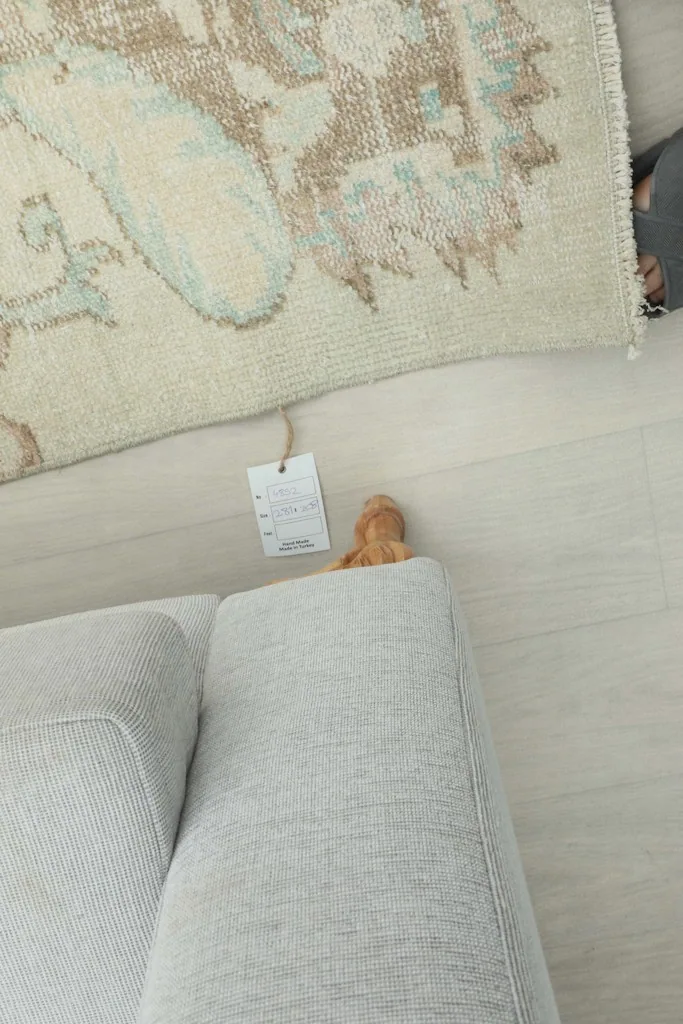 Close-up of the rug's edge and the small tag, positioned near a light-colored sofa