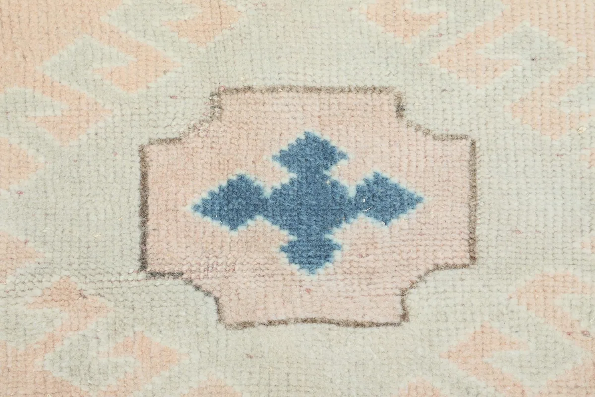 Close-up of a blue geometric motif within a rose shape on the beige field of the rug.