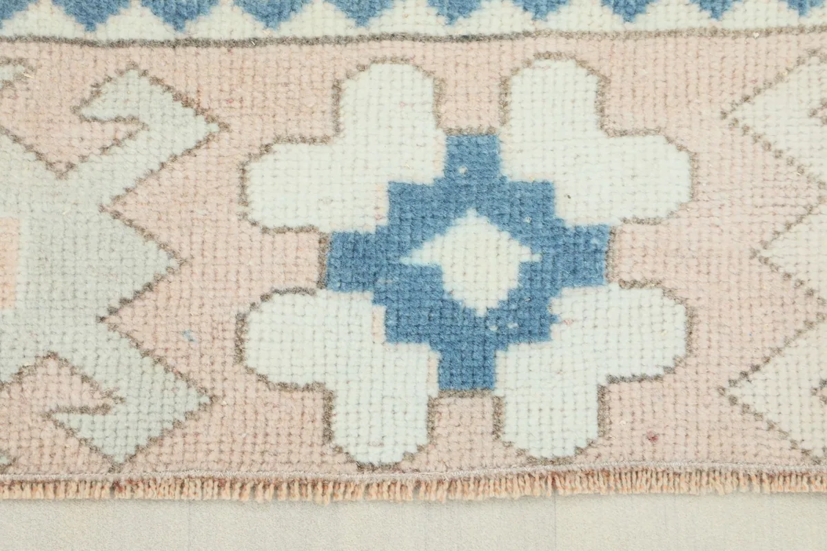 Close-up view of the rose border with blue and ivory geometric patterns on the vintage rug.