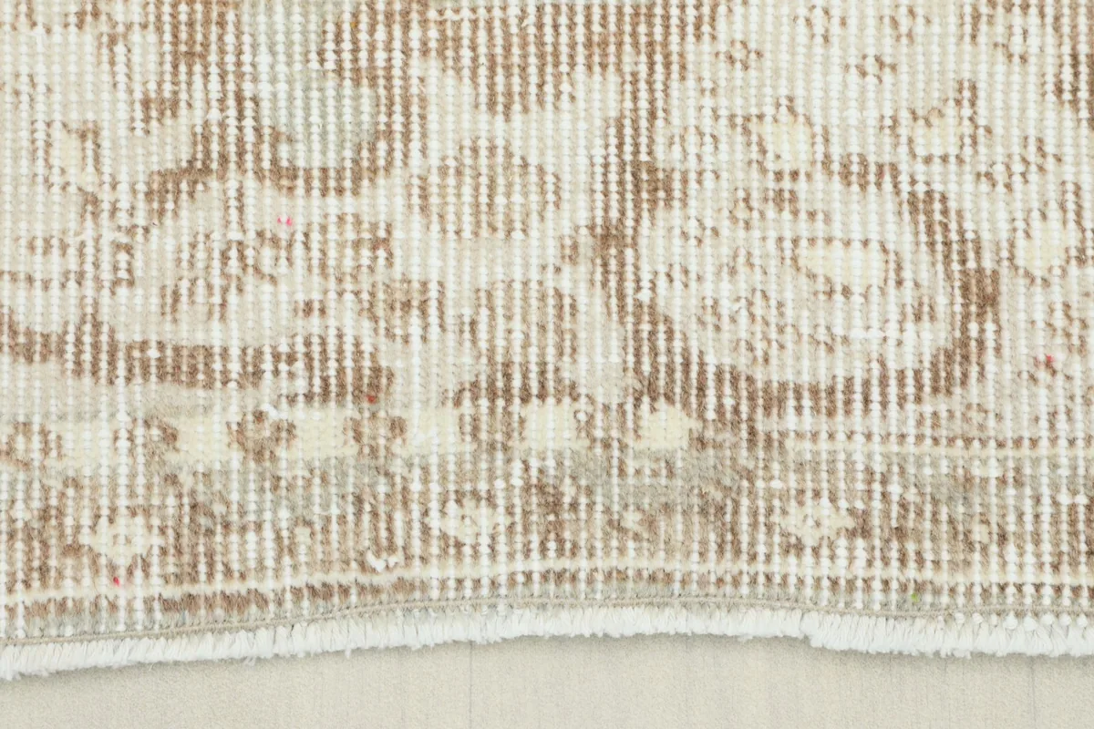 Close-up detail of the low pile texture and distressed beige floral patterns on the vintage rug.