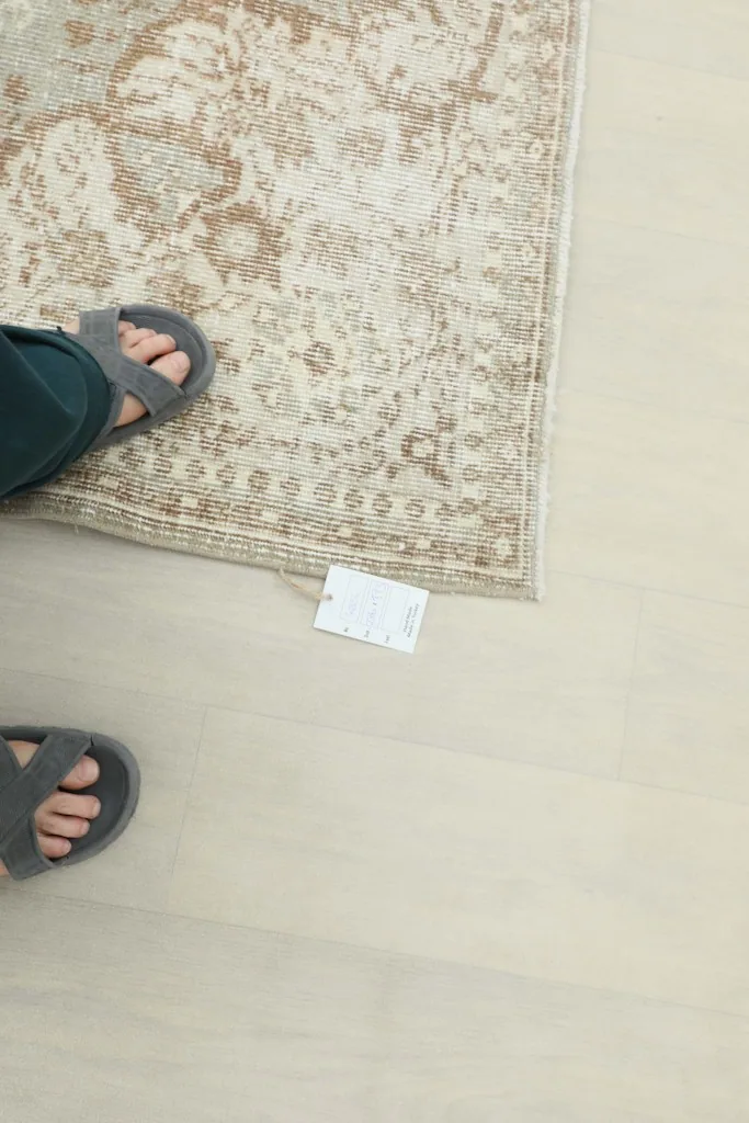 Feet standing on the rug next to a size tag, providing a sense of scale and texture.
