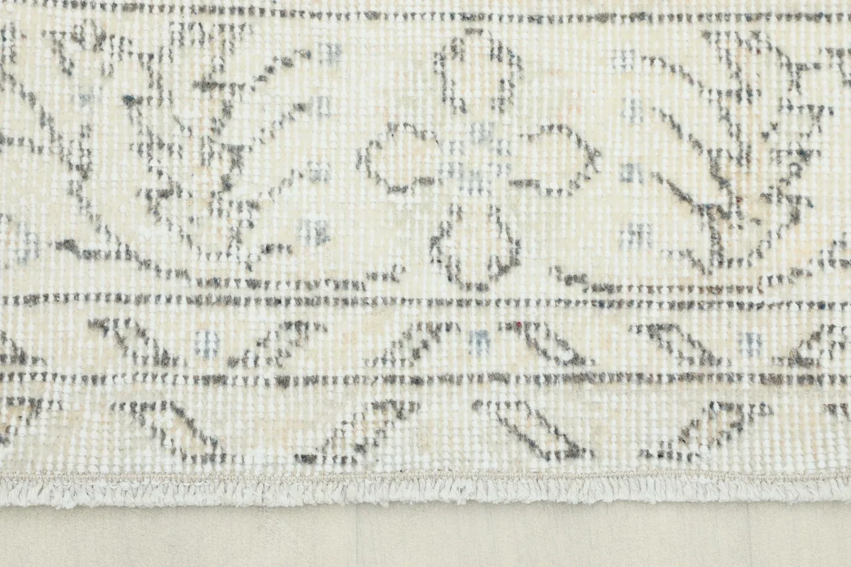 Close-up of the rug's border and fringe, highlighting the muted beige and gray floral details.