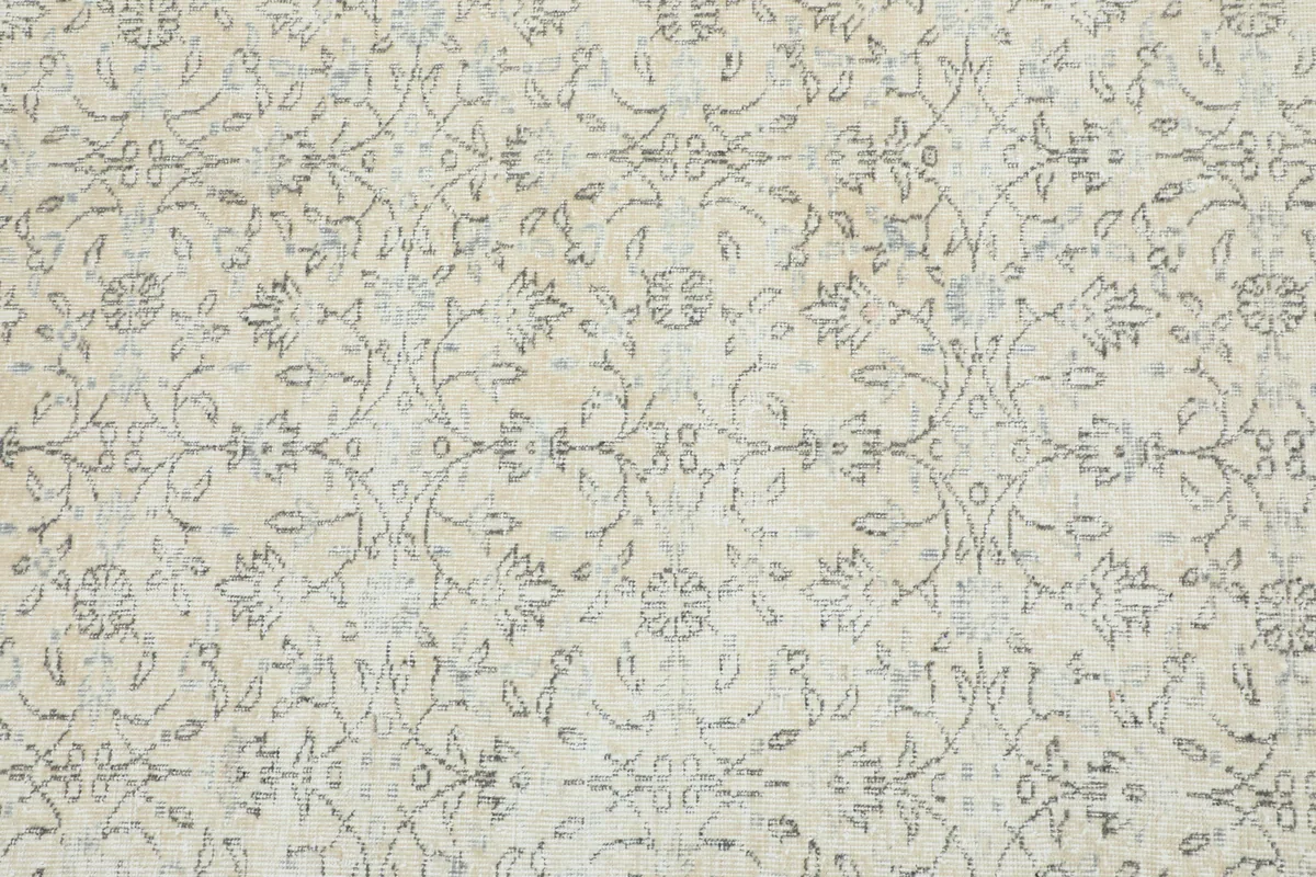 Detailed view of the rug's beige field with intricate gray floral and vine patterns.