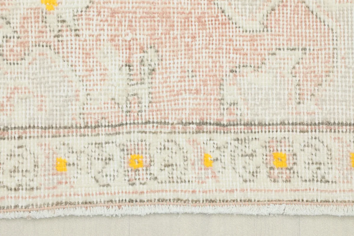 Close-up of the rug's border showing faded rose and ivory tones with yellow accents.
