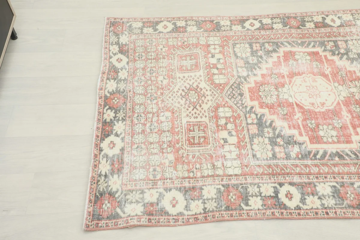 Angled view of the vintage rug highlighting the faded red and gray colors and overall pattern