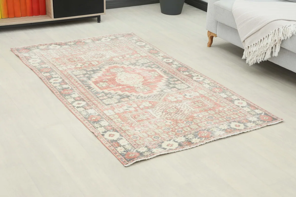 Angled view of the small red and gray vintage rug in a living room next to a light gray sofa