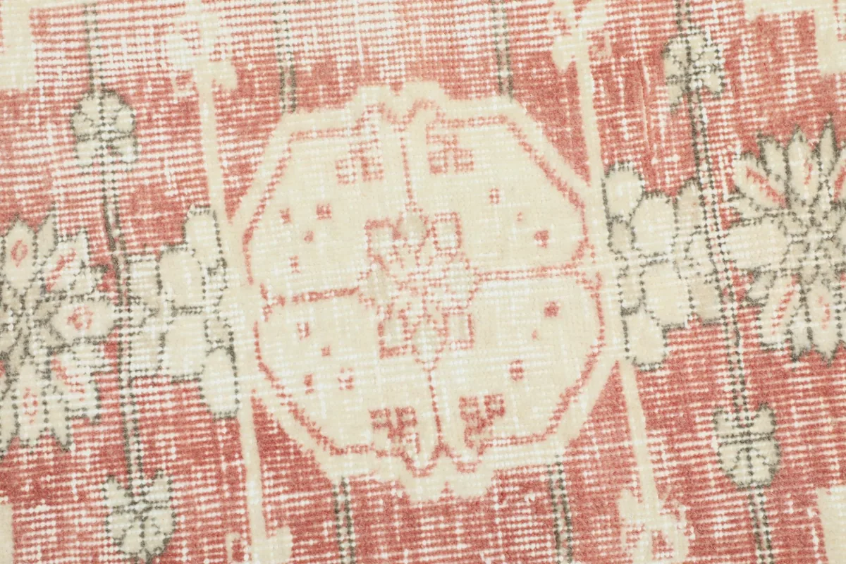 Close-up detail of the hand-knotted texture and faded red and ivory colors in the rug's pattern