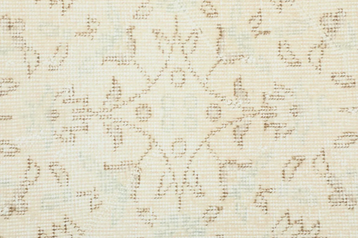 Macro detail of the hand-knotted wool pile and intricate floral design in beige and ivory