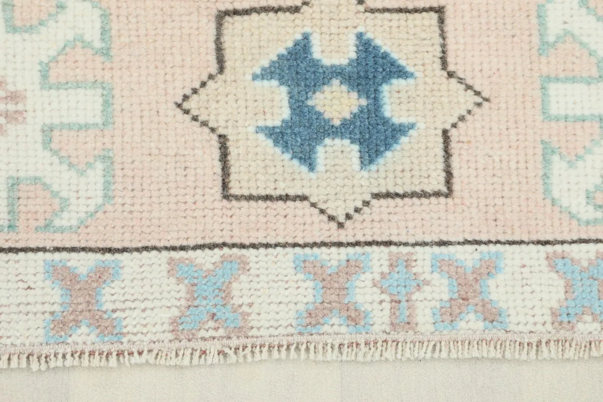 Close-up detail of the rose colored border with blue geometric motifs and short fringe