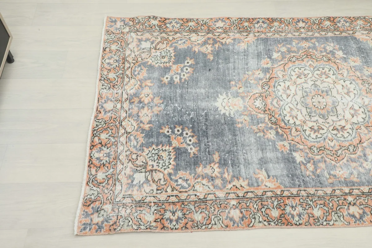 Overhead angle view highlighting the faded gray field and orange motifs of the rug