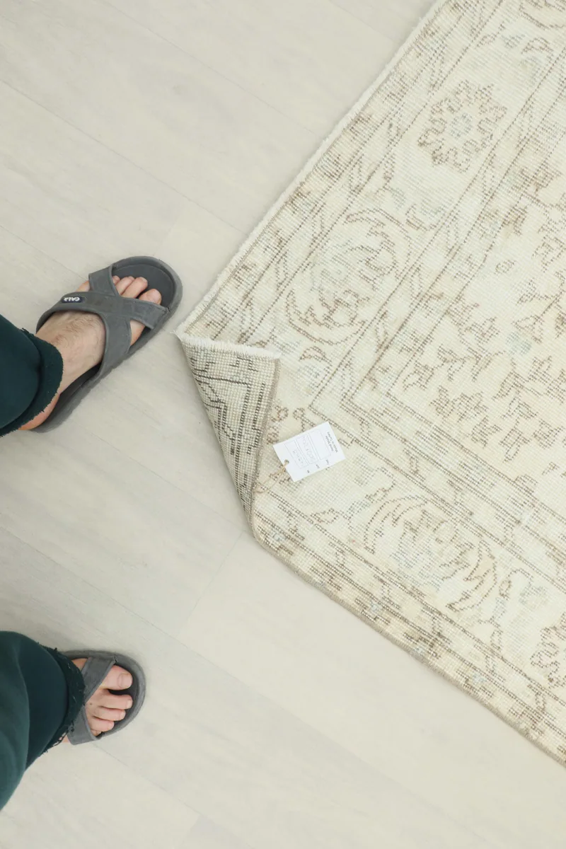 A person's feet on the Cream Floral Anatolian Rug, with a tag visible, for scale and texture reference