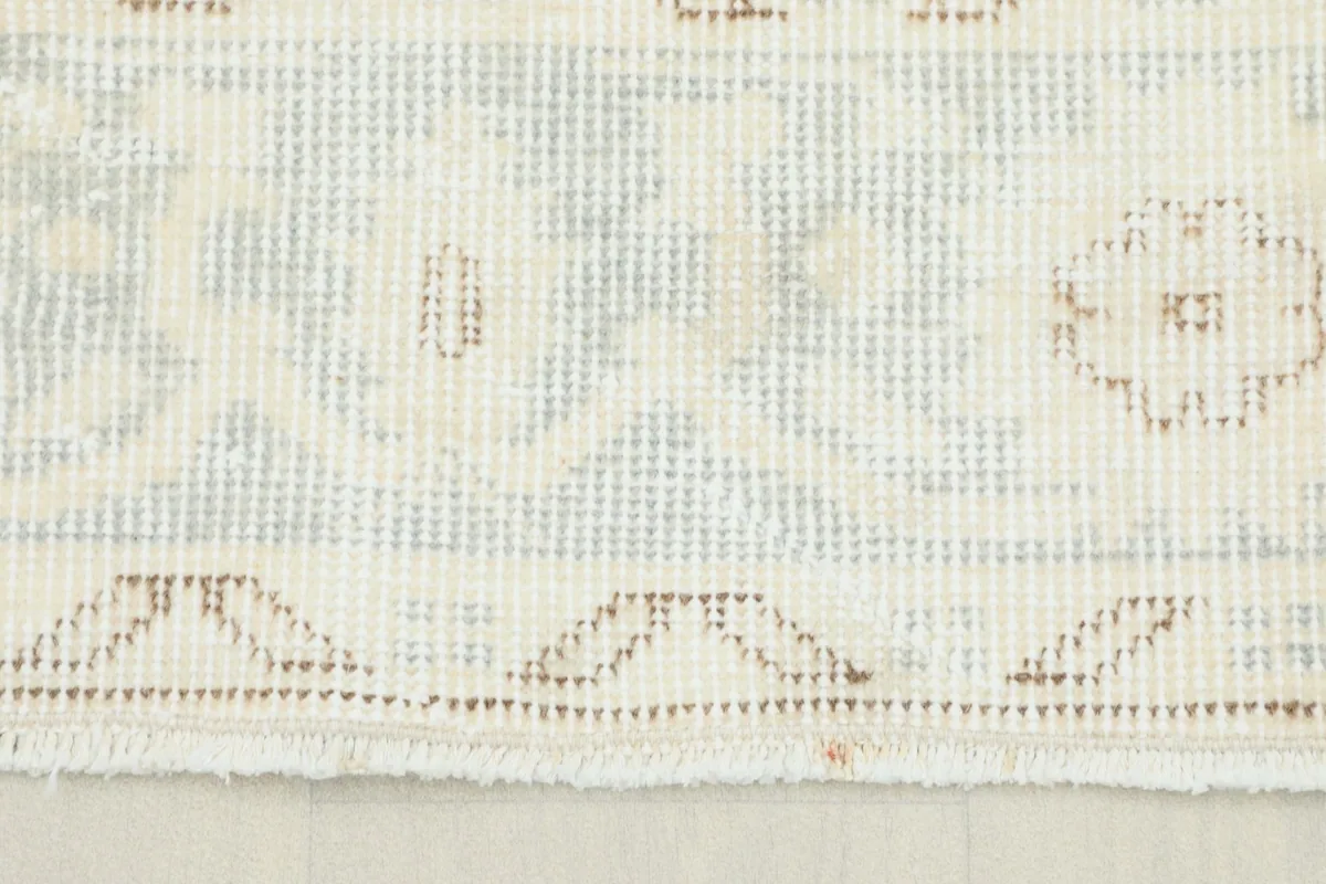 Close-up view of the rug's border showing faded tan and blue geometric patterns and low pile.