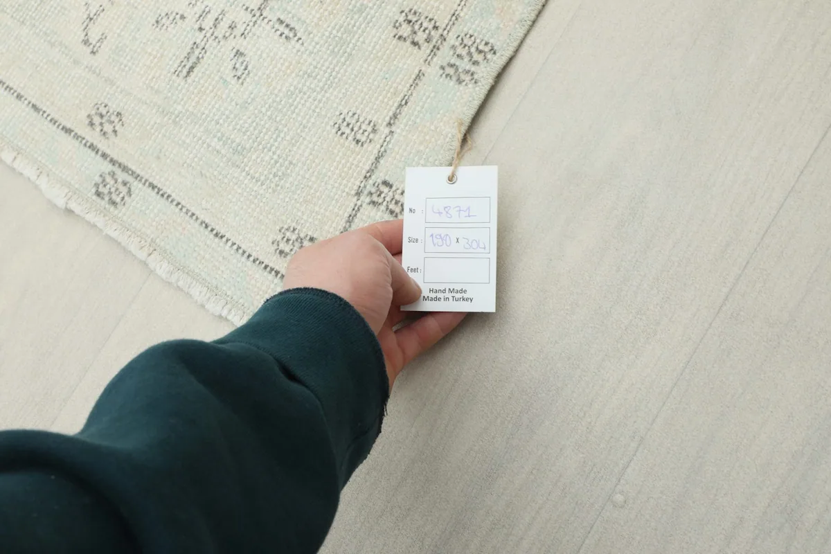 Hand holding a product tag, showing details and origin of the vintage Anatolian hand-knotted rug