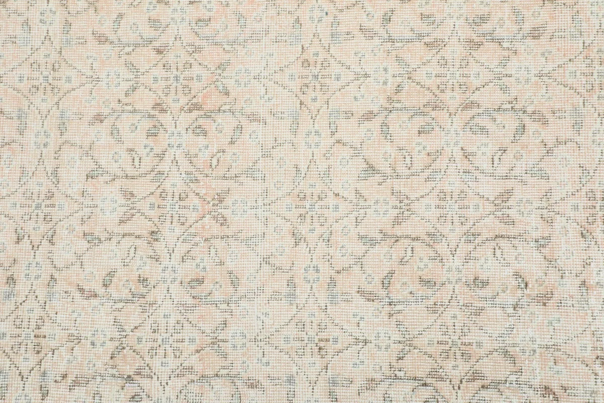 Detailed view of the ivory field and faded floral and geometric patterns of the rug