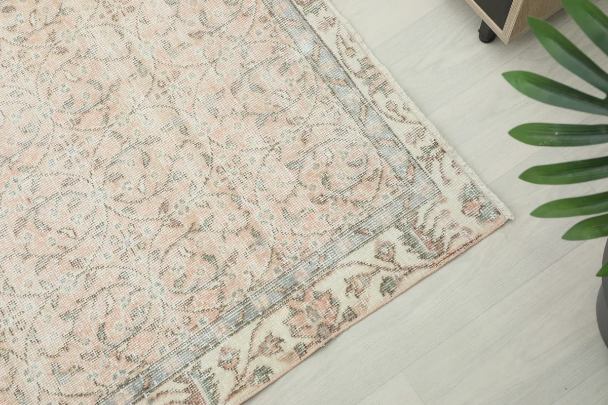 Angle view of the rug's border, featuring a delicate floral vine motif in gray and rose