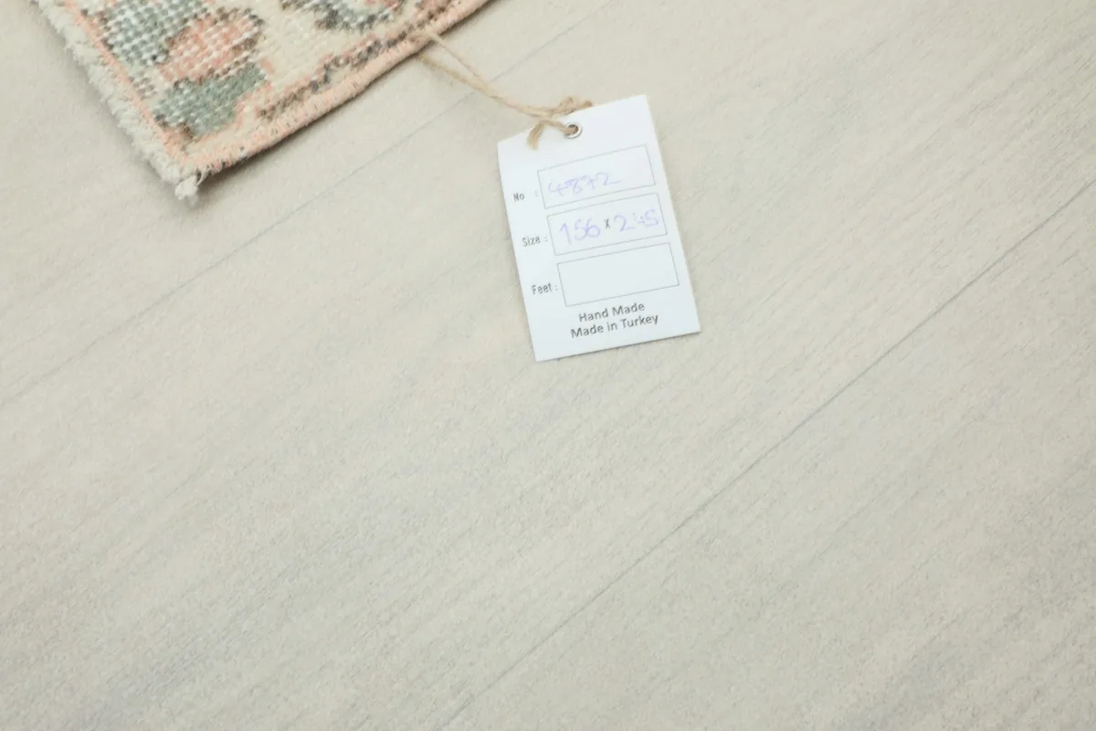 A tag attached to the rug, indicating it is hand-made in Turkey with size 156 x 245 cm