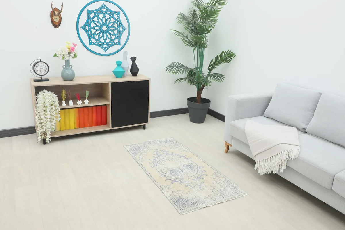Vintage beige and blue rug placed in a living room setting next to a sofa and cabinet