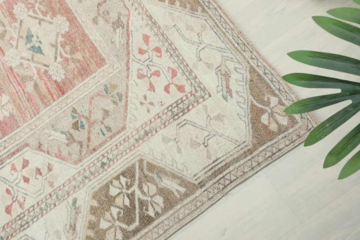 Angled view showcasing the beige border with brown tribal motifs and a corner of the rug