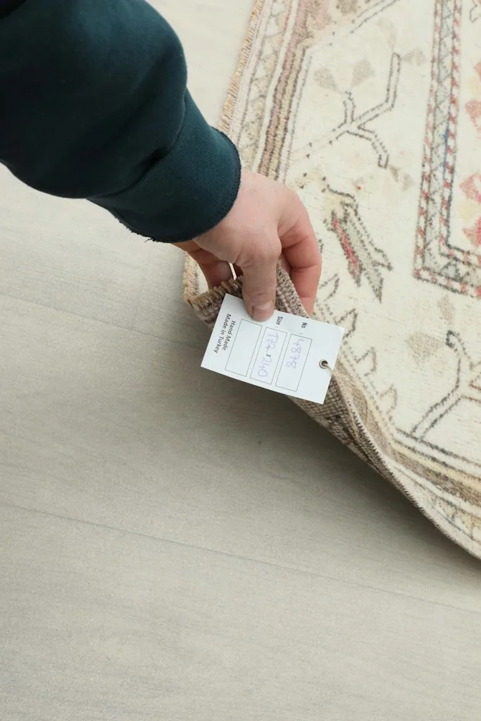 A hand holding a tag attached to the corner of the vintage hand-knotted rug