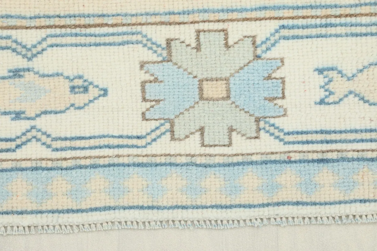 Close-up detail of the ivory border with blue geometric and fish motifs on the vintage rug