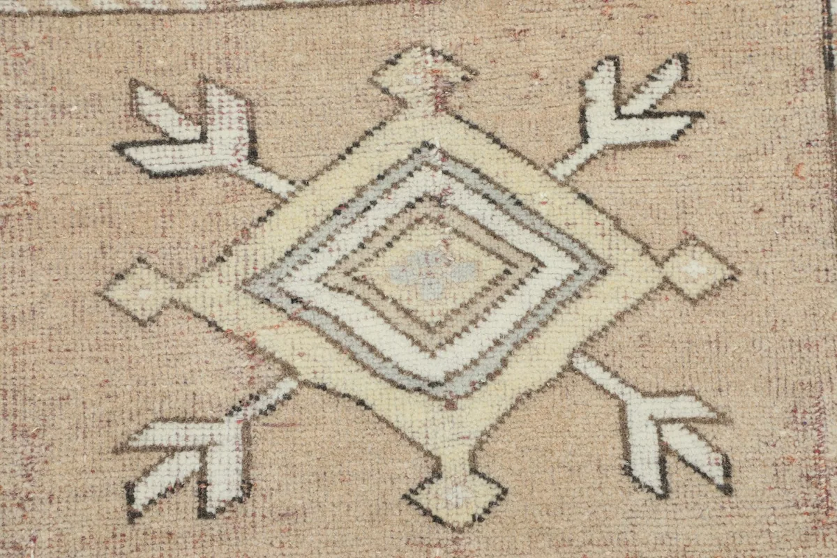 Close-up of a distinct geometric medallion pattern in cream and gray on the rug's rose field.