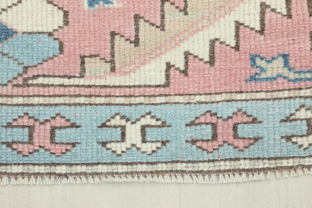 Close-up view of the rug's outer border showing light blue, rose, and ivory geometric patterns