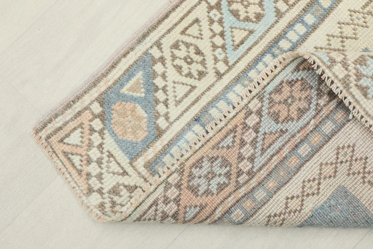 Corner of the ivory and blue rug folded back, showing the back of the hand-knotted foundation