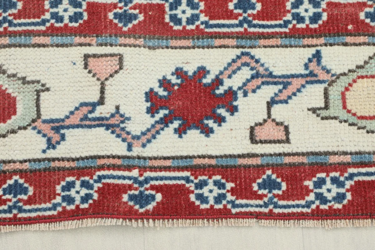 Close-up of the rug's red and ivory border with blue and pink tribal motifs.