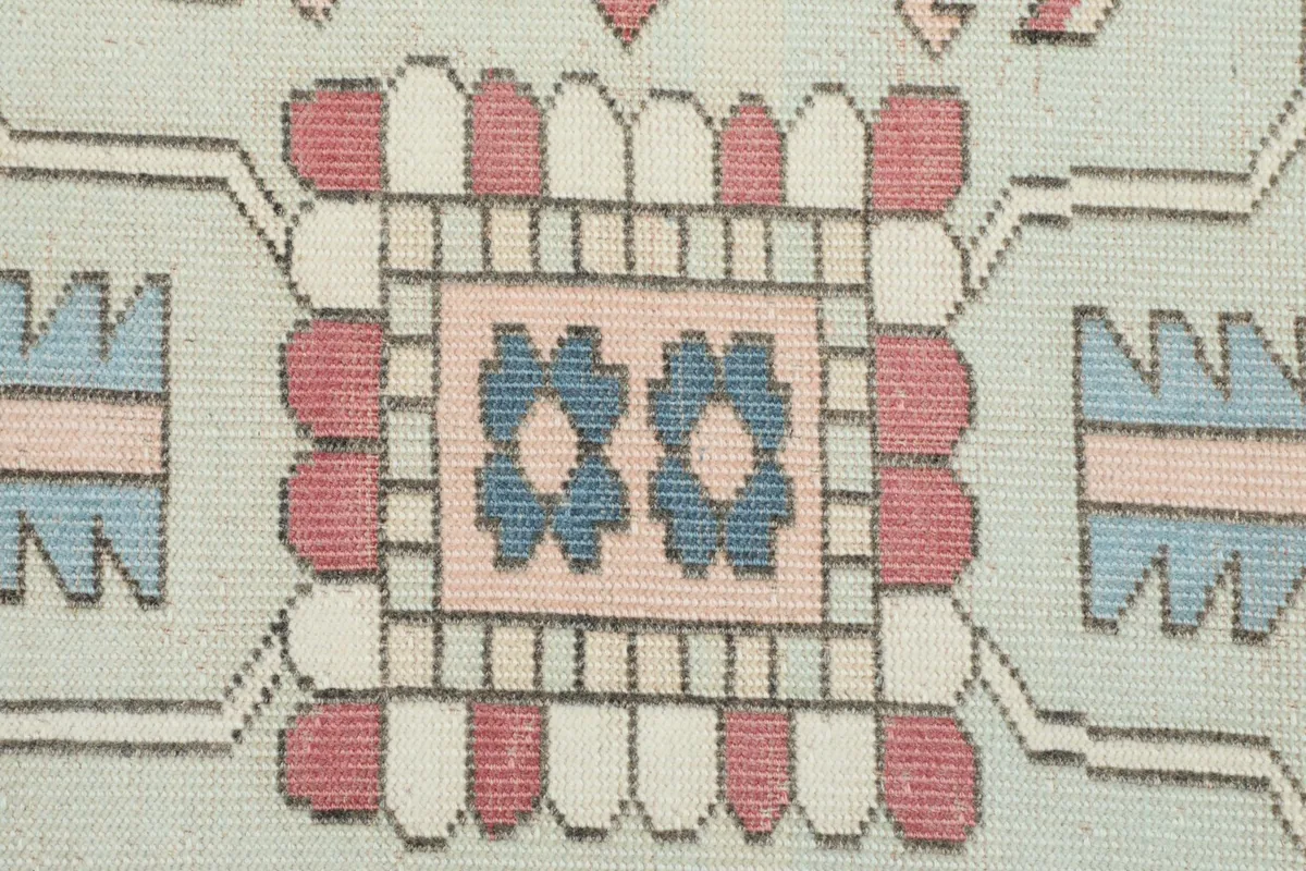 Close-up of a blue and pink geometric motif within the rug's design, highlighting knotting.