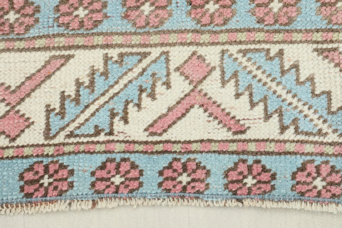 Close-up of the rug's border showing blue, rose, and ivory geometric and floral patterns